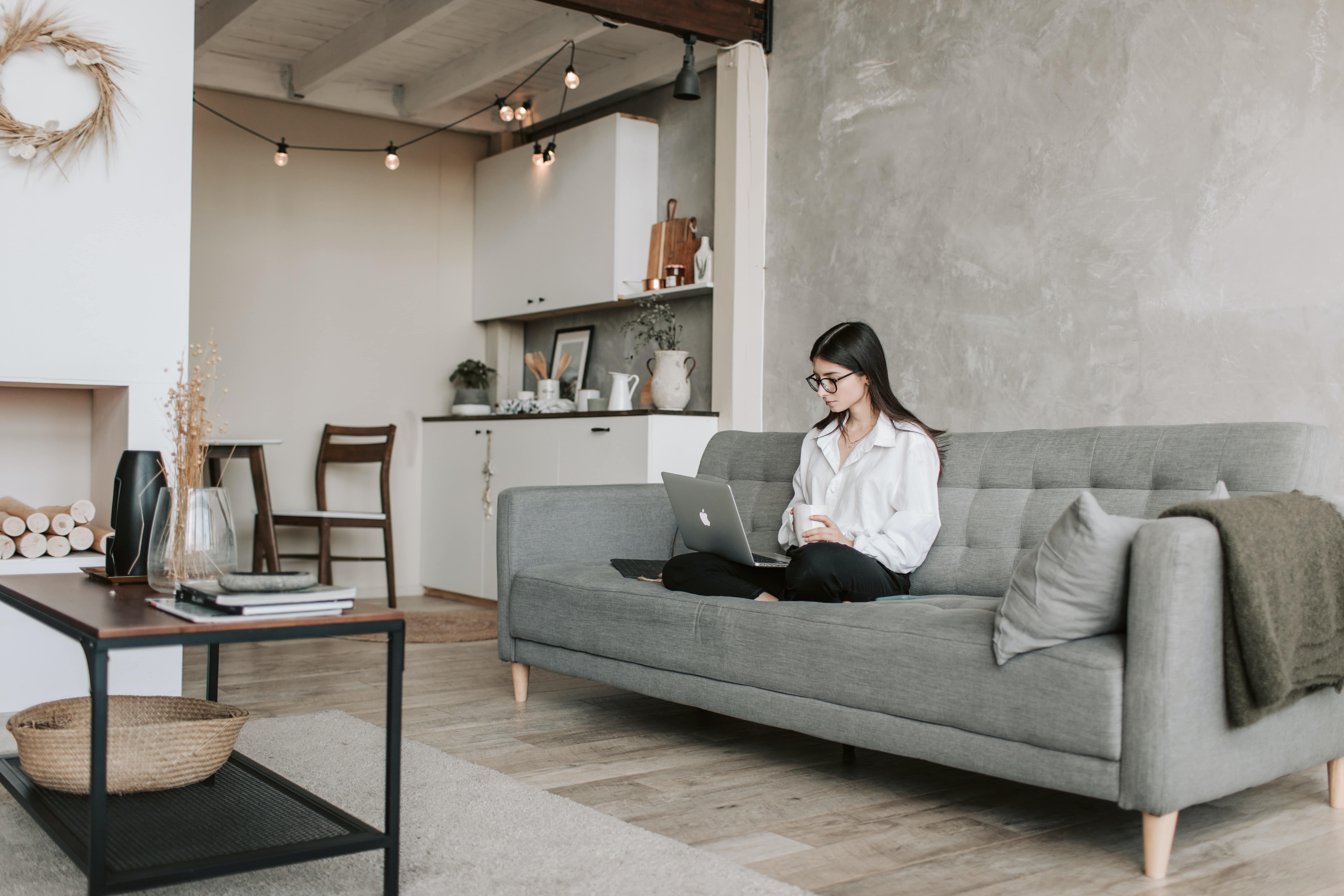 woman sitting on a couch while working on laptop