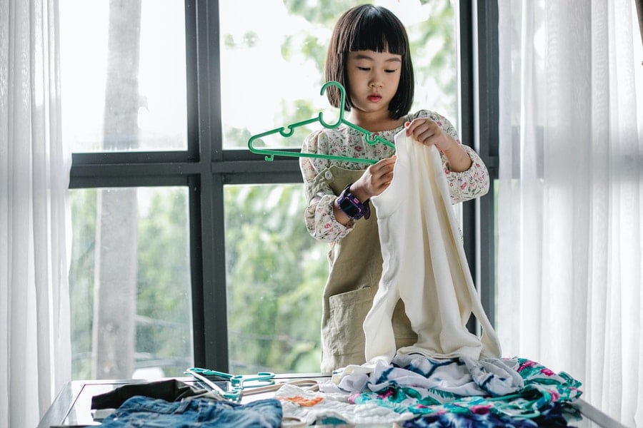 A kid putting a clother on a clothe hanger