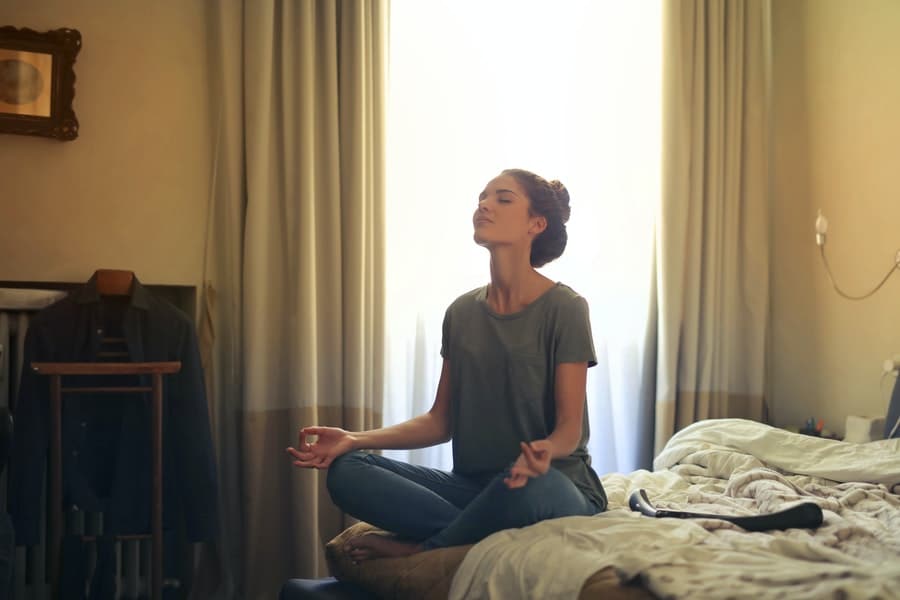 A woman sitting on a bed while doing yoga 