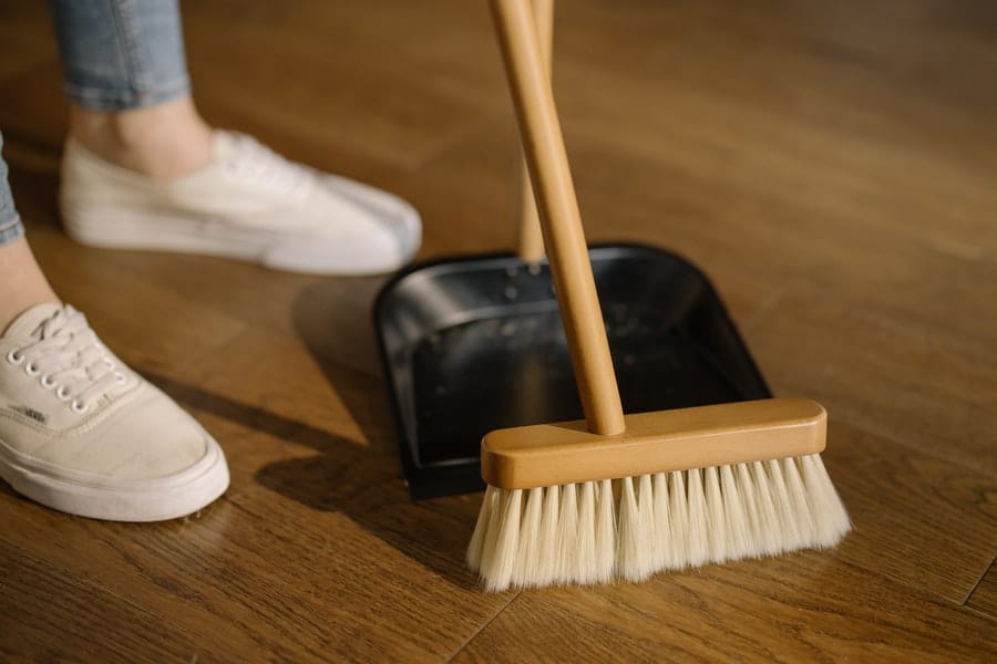 Person wearing pants and white shoes standing behind brown broom