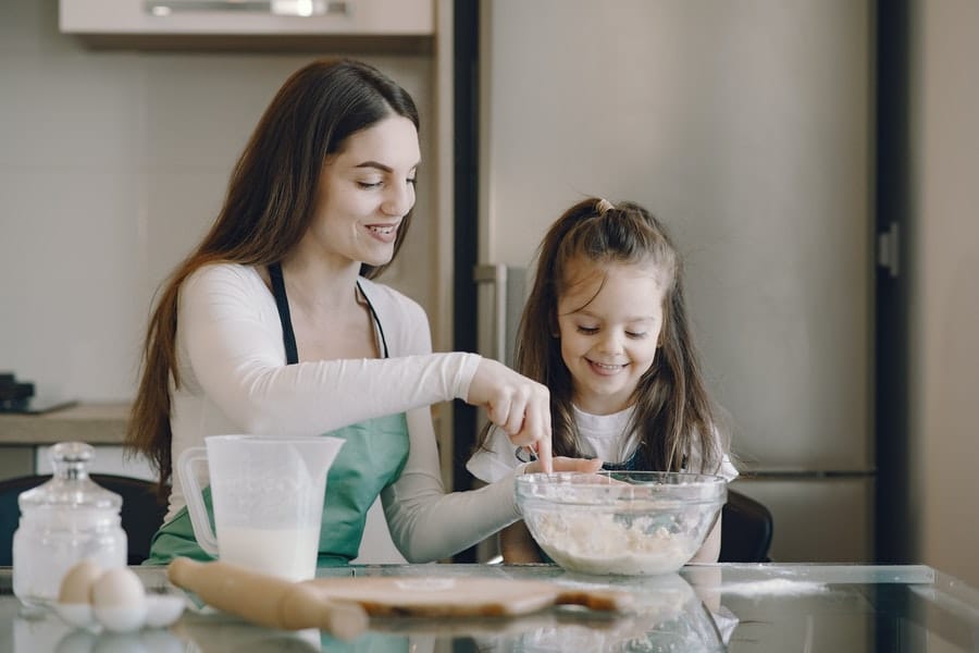 Mom in apron teaches her daughter how to bake