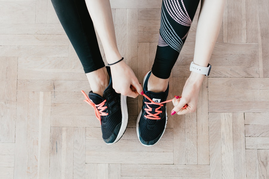 A person in workout pants tidying up the lace of her rubber shoes.