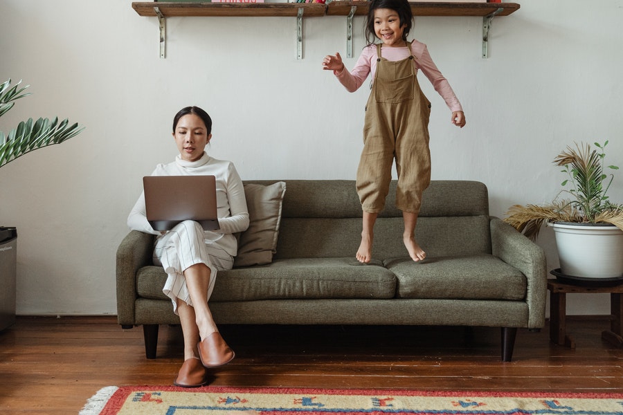 A woman working on a couch and a little girl playing beside her