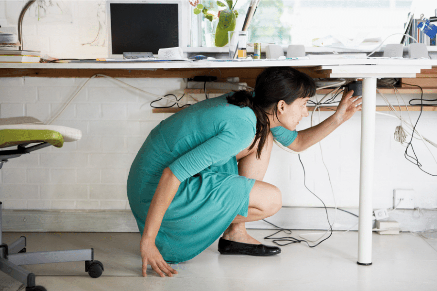 A woman crouching under her desk organizing computer cables